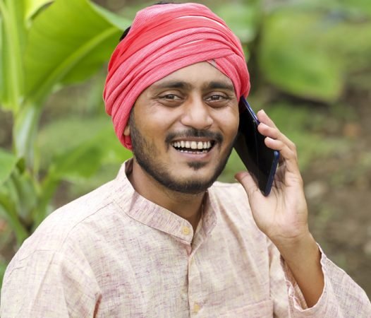 Young indian farmer talking on smartphone at banana agriculture field.